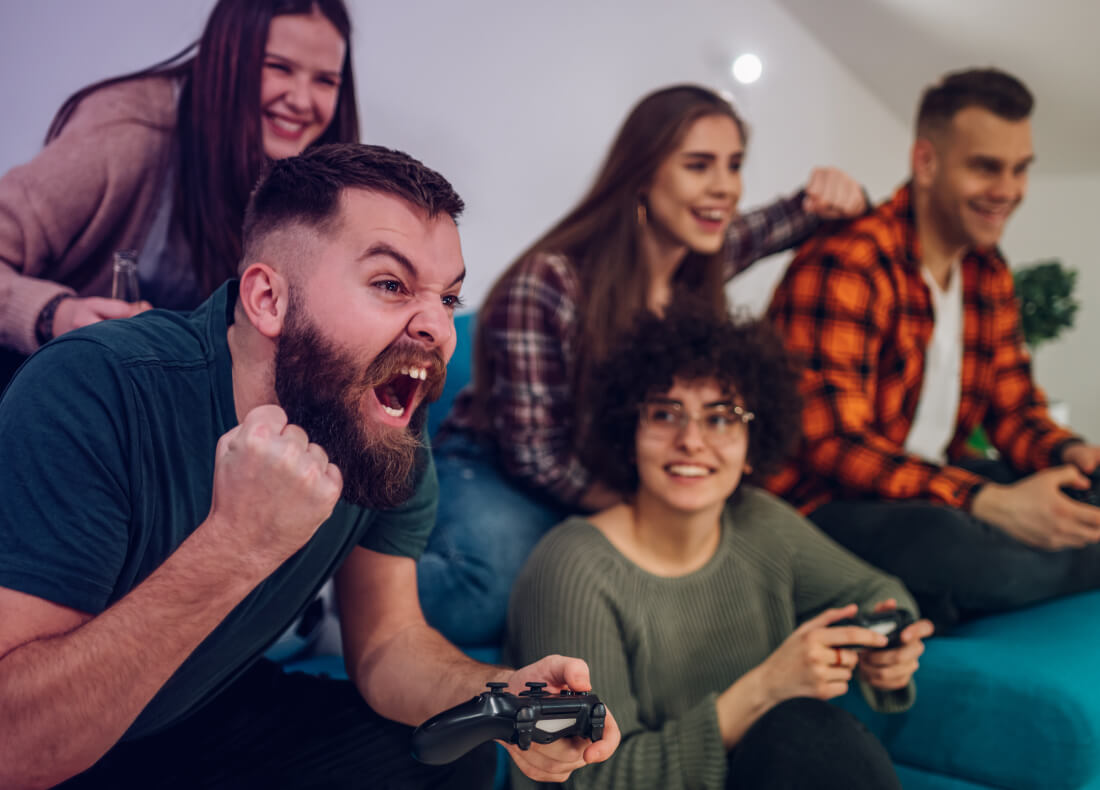 A group of people playing video games while a friend gets excited about their win 