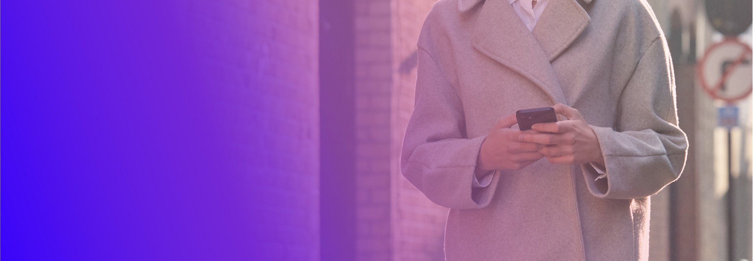 امرأة ترتدي معطفًا تمشي وهي تحمل هاتفًا محمولاً في يدها