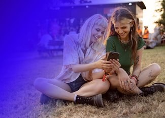Two happy girls laying in the grass and looking at their phone